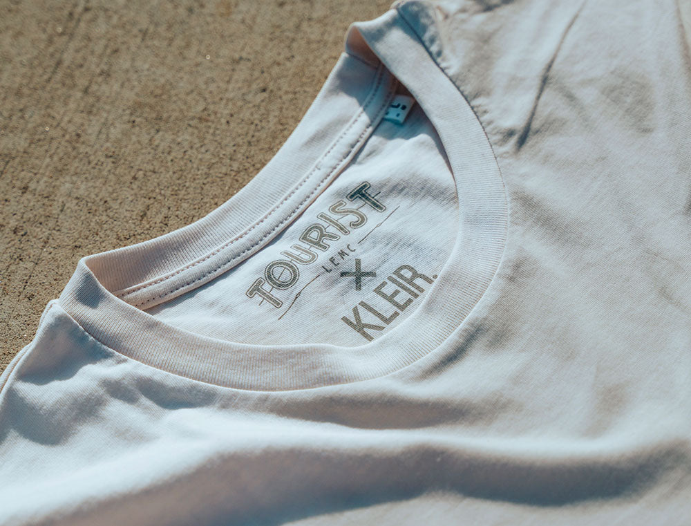 Close-up van witte T-shirt nek met logo TOURIST en KLEIR.