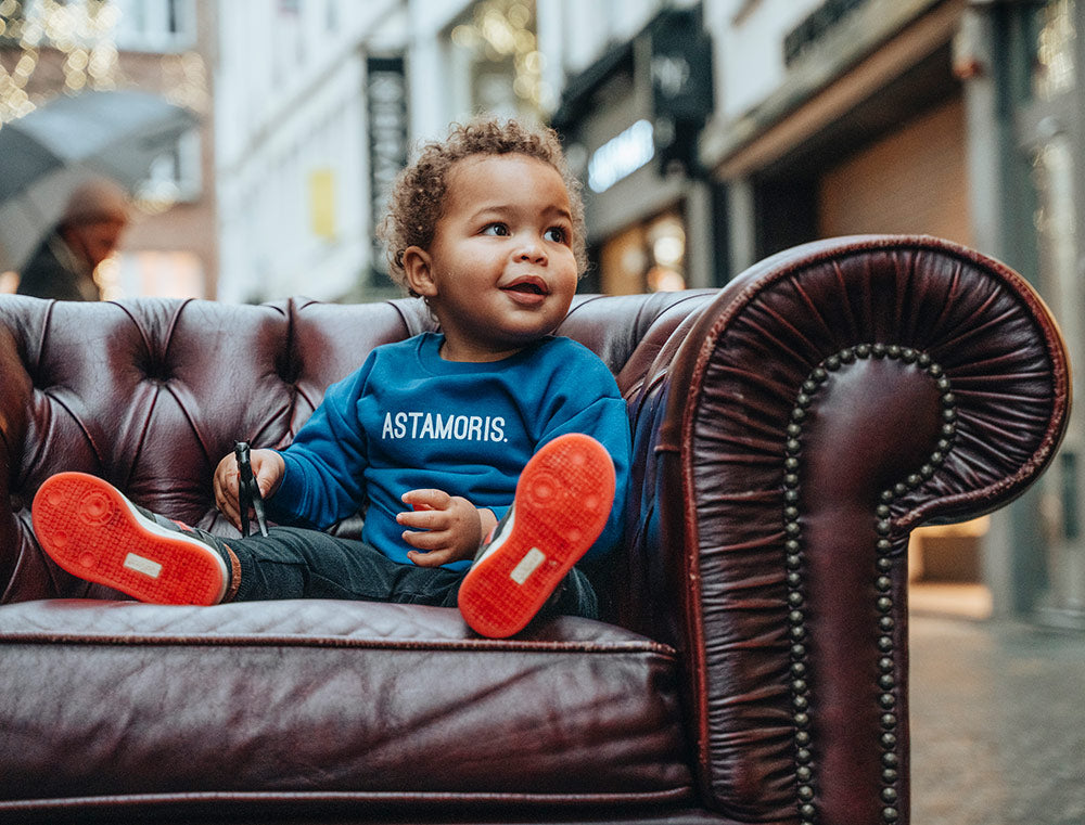 Baby met een blauwe baby-trui met opdruk ASTAMORIS.