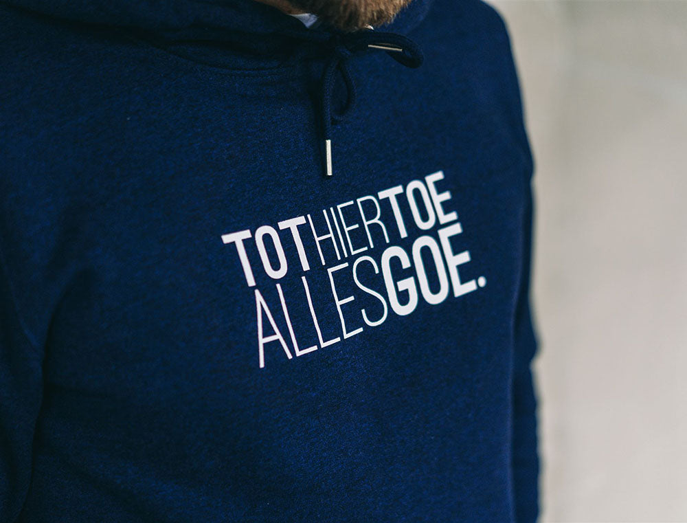 Close-up van een donkerblauwe hoodie met opdruk TOTHIERTOEALLESGOE.