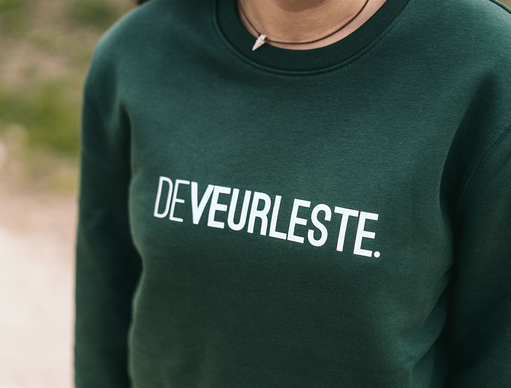 Close-up van een groene trui met opdruk DEVEURLESTE.