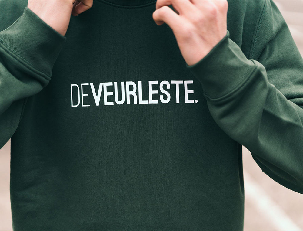 Close-up van een groene trui met opdruk DEVEURLESTE.