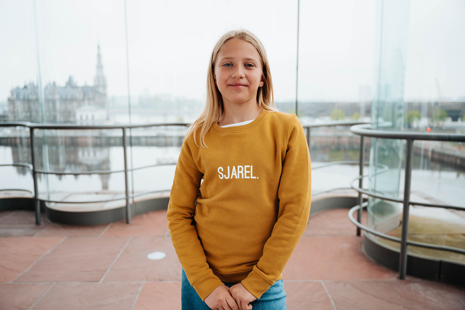 Meisje met okerkleurige trui met opdruk SJAREL.