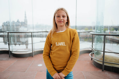 Meisje met okerkleurige trui met opdruk SJAREL.