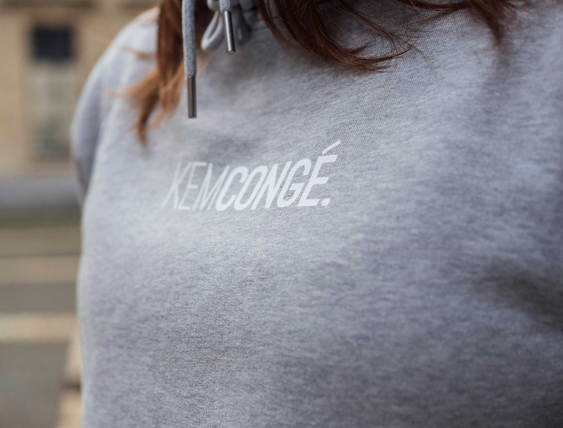 Close-up van een grijze hoodie met opdruk KEMCONGE.