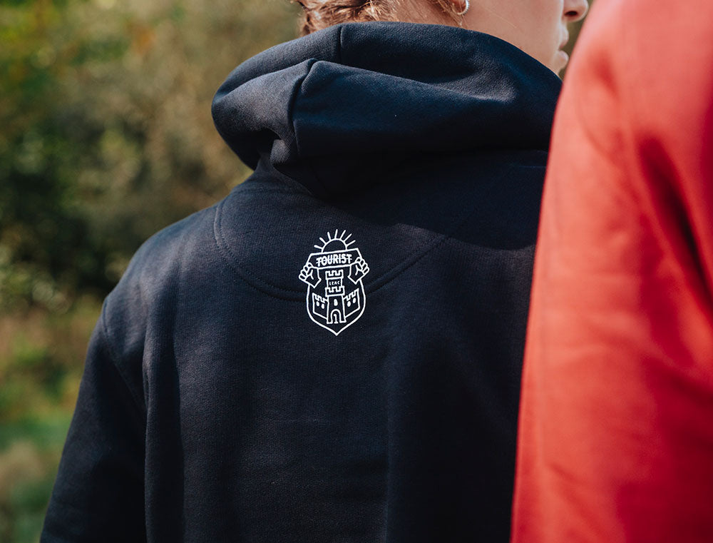 Achterkant van zwarte hoodie met logo van TOURIST