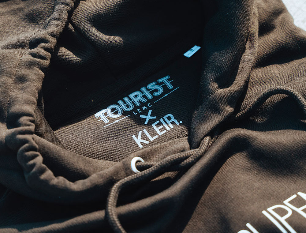 Close-up van zwarte hoodie nek met logo van TOURIST en KLEIR.