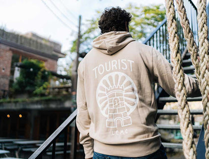 Een man met de achterkant van een zandkleurige hoodie met een illustratie.