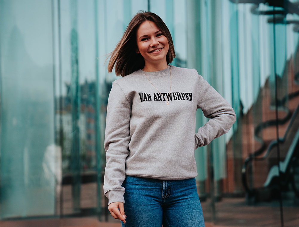 Vrouw met een grijze trui met opdruk 'VAN ANTWERPEN'