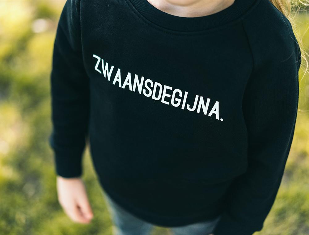 Close-up van zwarte trui met opdruk ZWAANSDEGIJNA.