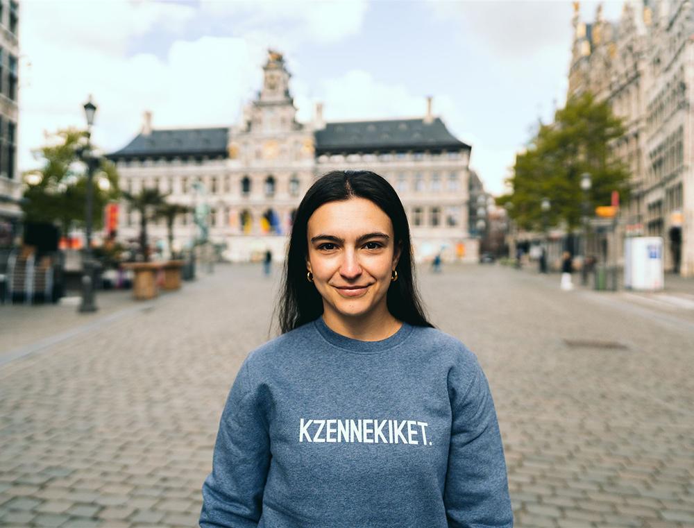 Zwartharige vrouw met blauw-grijze trui met opdruk 'KZENNEKIKET.'