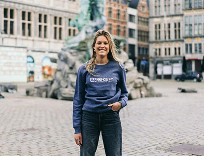 Blonde vrouw met blauw-grijze trui met opdruk 'KZENNEKIKET.'