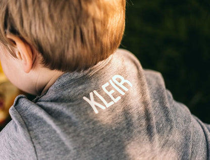 Close-up van een jongen met een grijze T-shirt met KLEIR op de nek gedrukt
