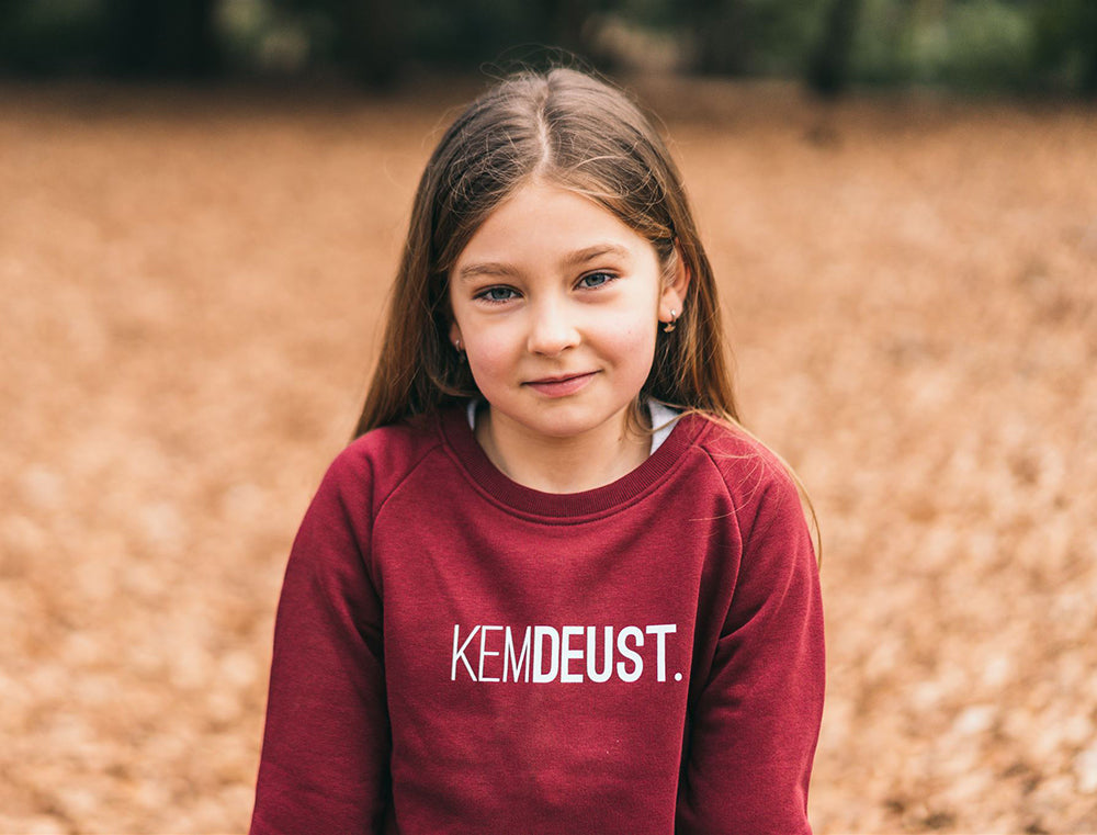 Meisje met een bordeaux trui met opdruk KEMDEUST.