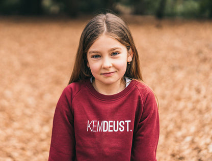 Meisje met een bordeaux trui met opdruk KEMDEUST.
