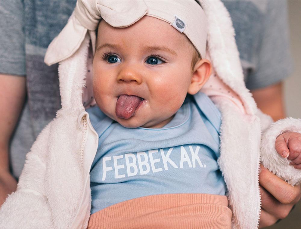 Baby met blauw rompertje met opdruk FEBBEKAK..