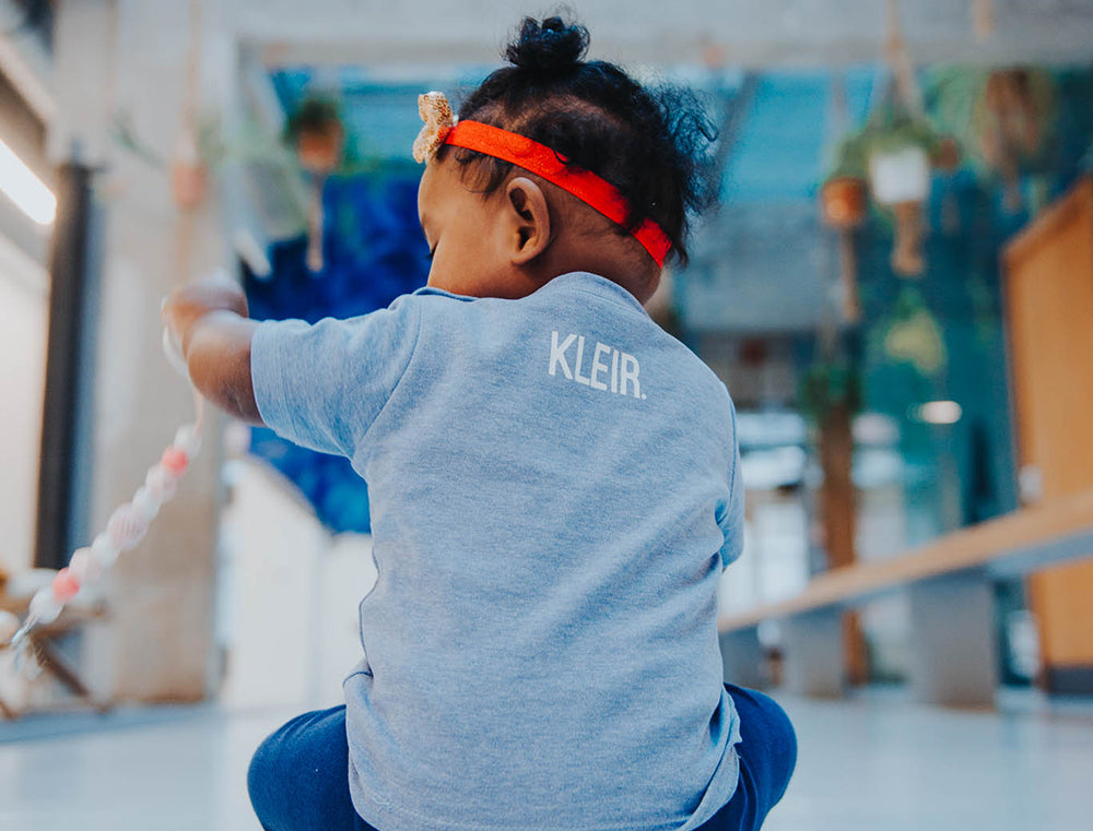 Close-up van blauwe baby T-shirt met opdruk KLEIR. in de nek.