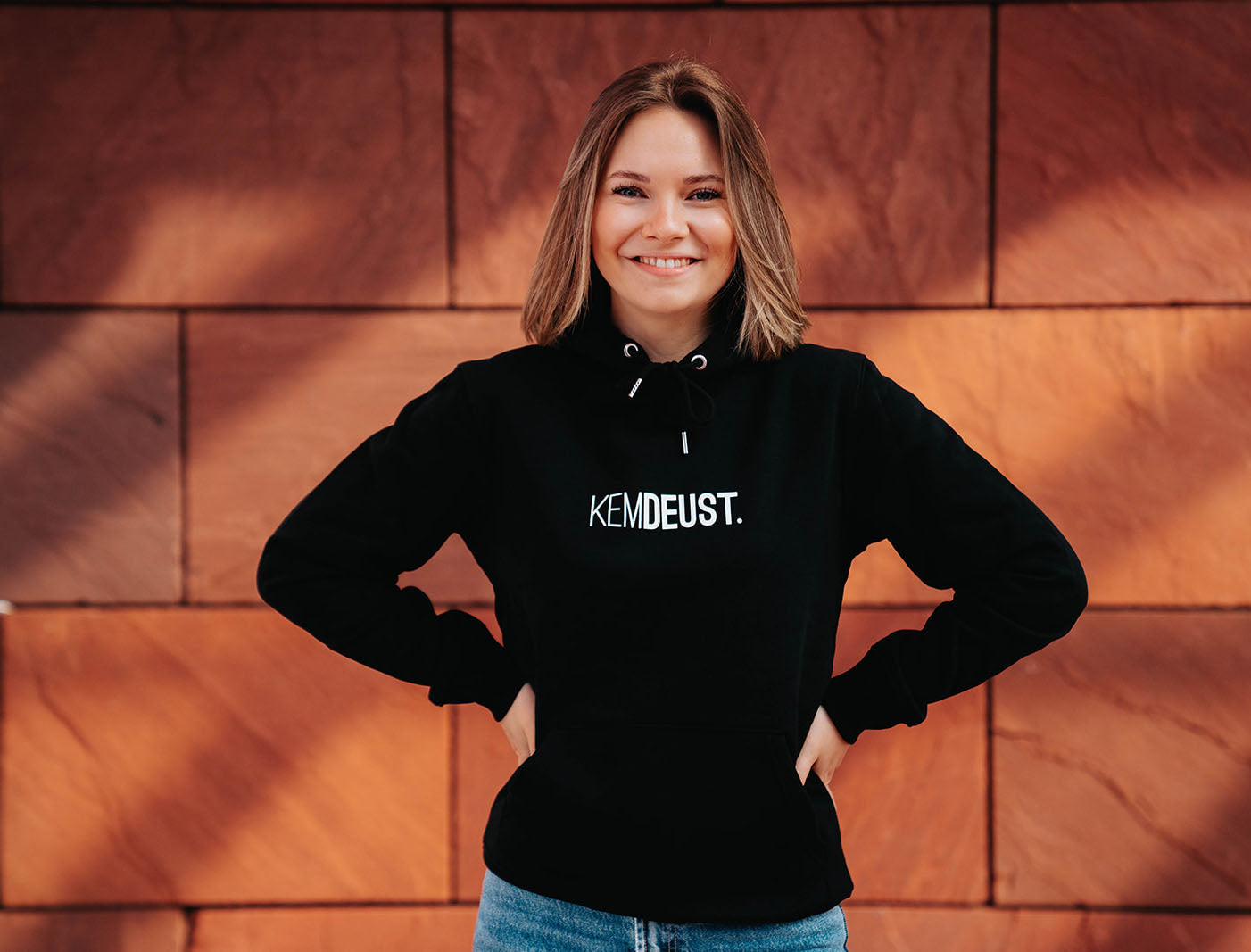 Vrouw met een zwarte hoodie met opdruk KEMDEUST.
