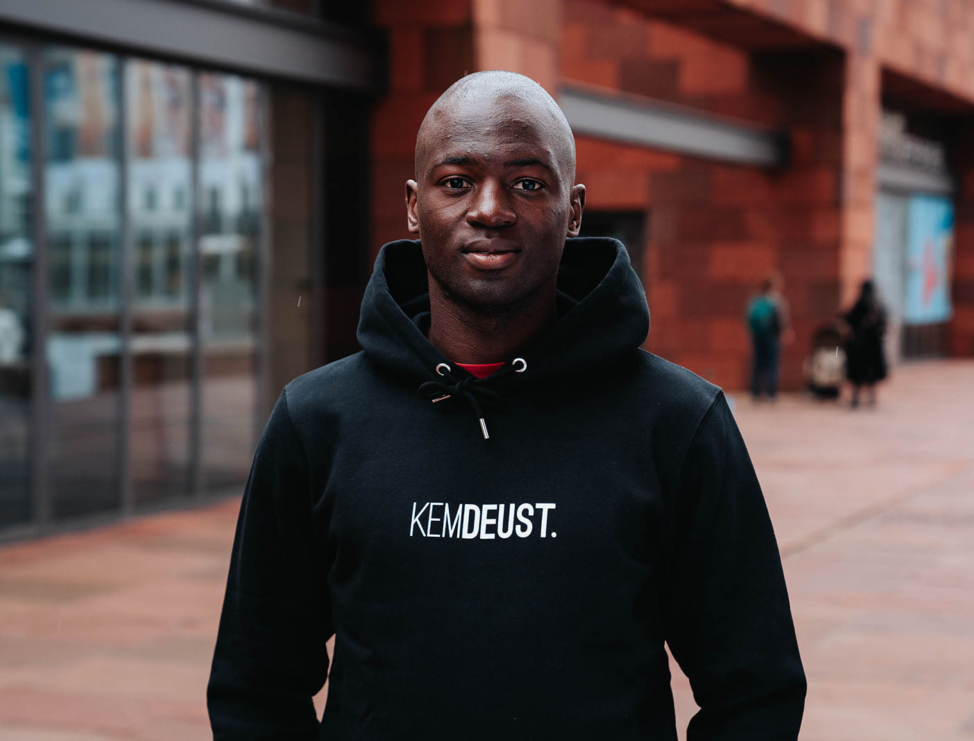 Man met een zwarte hoodie met opdruk KEMDEUST.