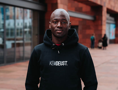 Man met een zwarte hoodie met opdruk KEMDEUST.