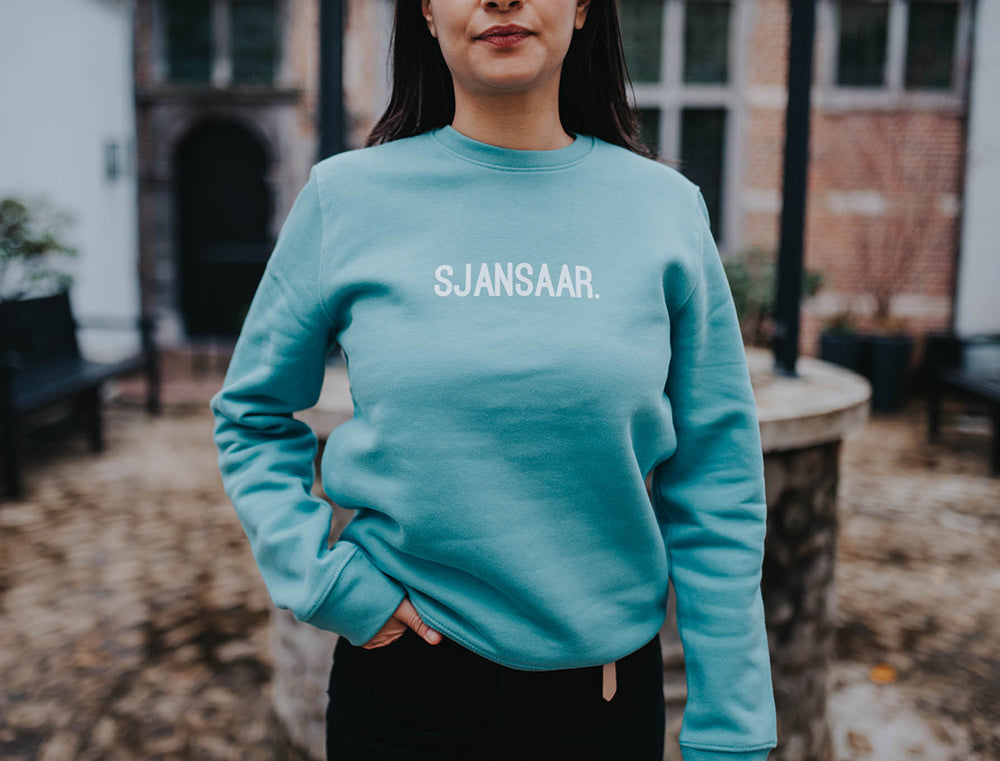 Close-up van een blauw-groene trui met opdruk SJANSAAR.
