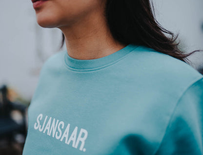 Close-up van een blauw-groene trui met opdruk SJANSAAR.