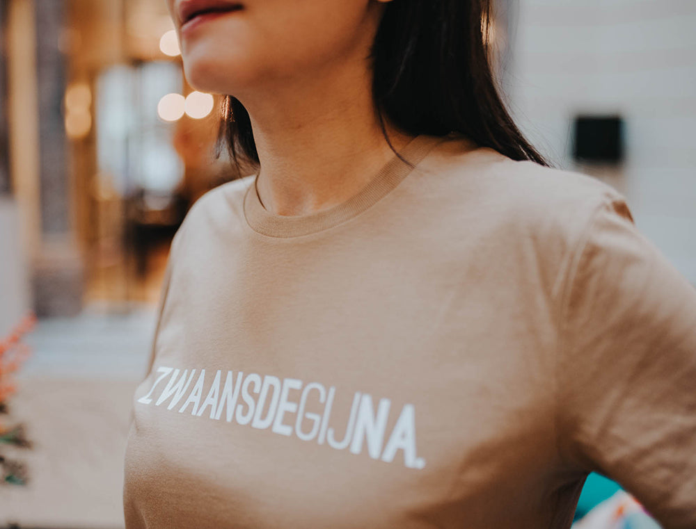 Close-up van een bruine T-shirt met opdruk ZWAANSDEGIJNA.
