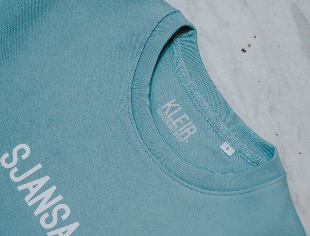 Close-up van een blauw-groene trui met opdruk SJANSAAR.