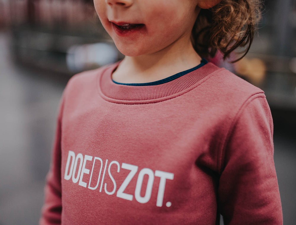 Close-up van een bordeaux trui met opdruk DOEDISZOT.