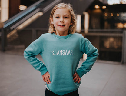 Meisje met een blauw-groene trui met opdruk SJANSAAR.