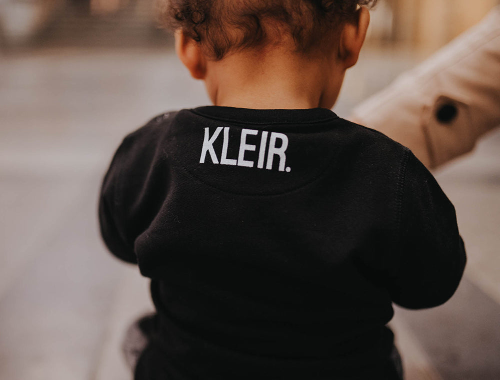 Close-up van zwarte baby trui met logo van KLEIR.