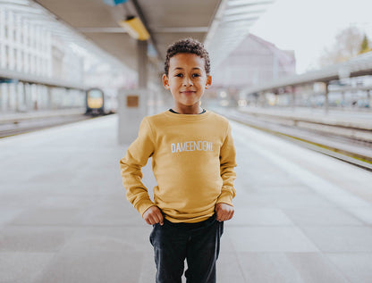 Jongen met okerkleurige trui met opdruk DAMEENDENI.