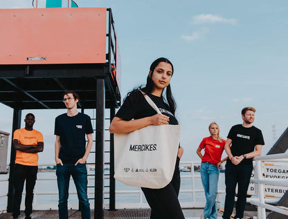 Mensen met vrouw in het midden met een totebag met opdruk MERCIKES.